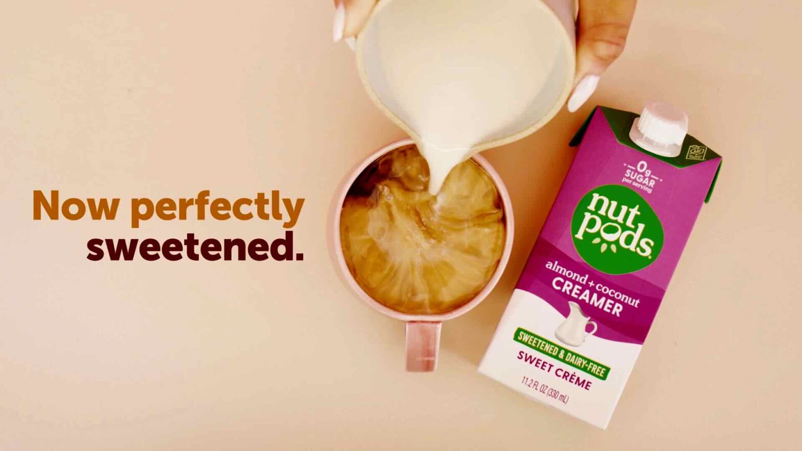 A carton of nutpods almond and coconut creamer is on a table next to a cup, with creamer being poured into the cup. The text reads, "Now perfectly sweetened." This captivating image could be a cornerstone of any content marketing campaign.